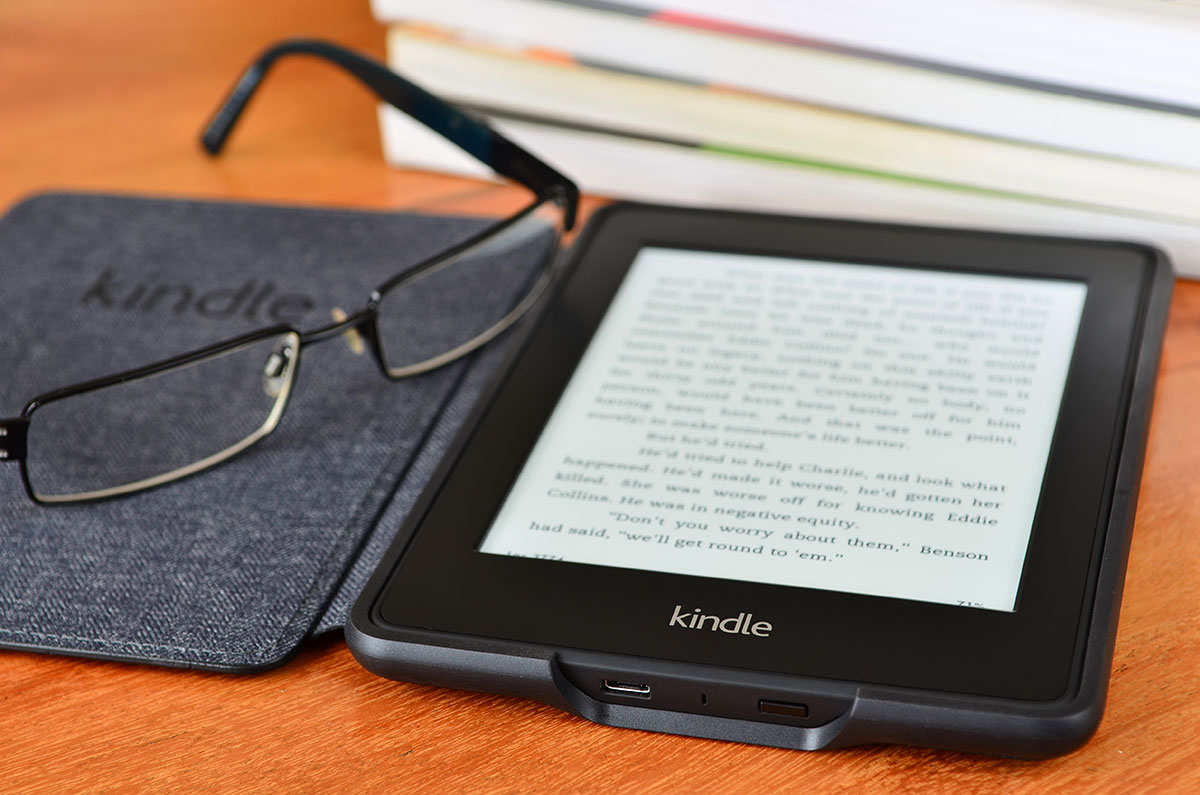 Kindle e-reader and eyeglasses on a wooden table