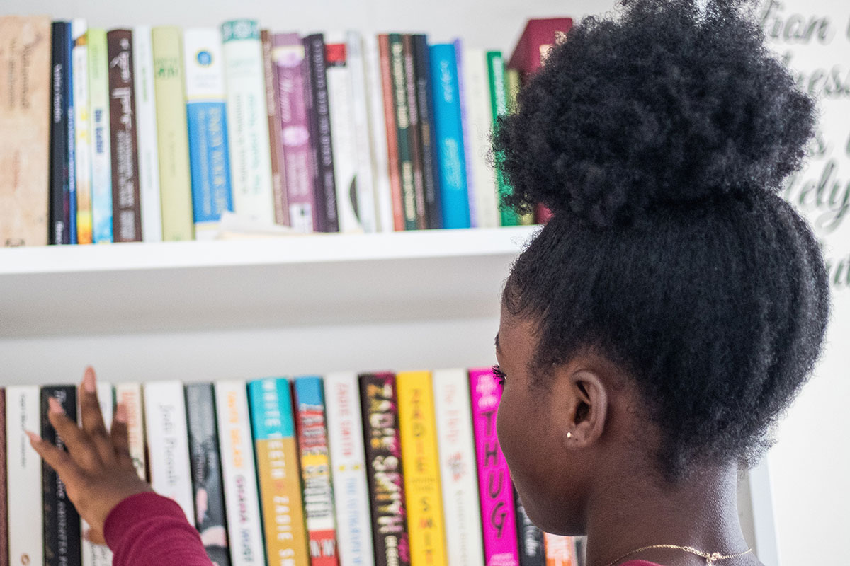 Young Black girl browses books on shelf