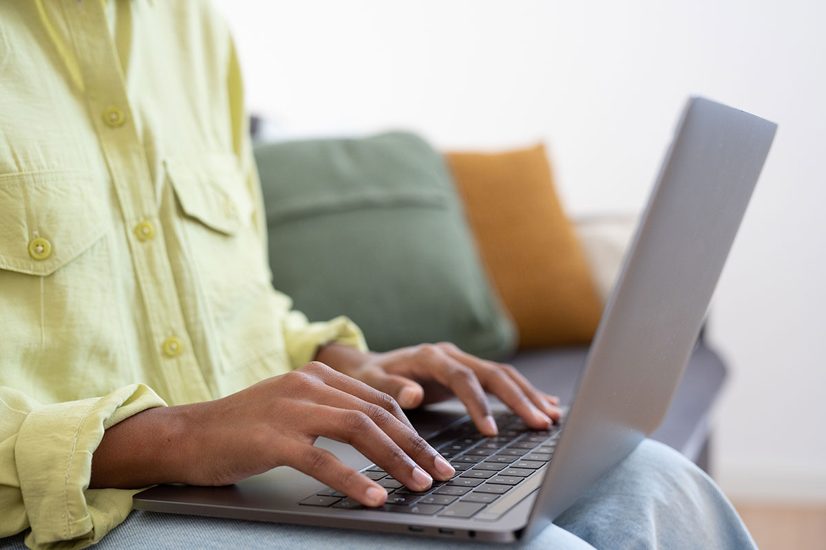 Closeup of woman wearing a yellow shirt writing at a laptop computer