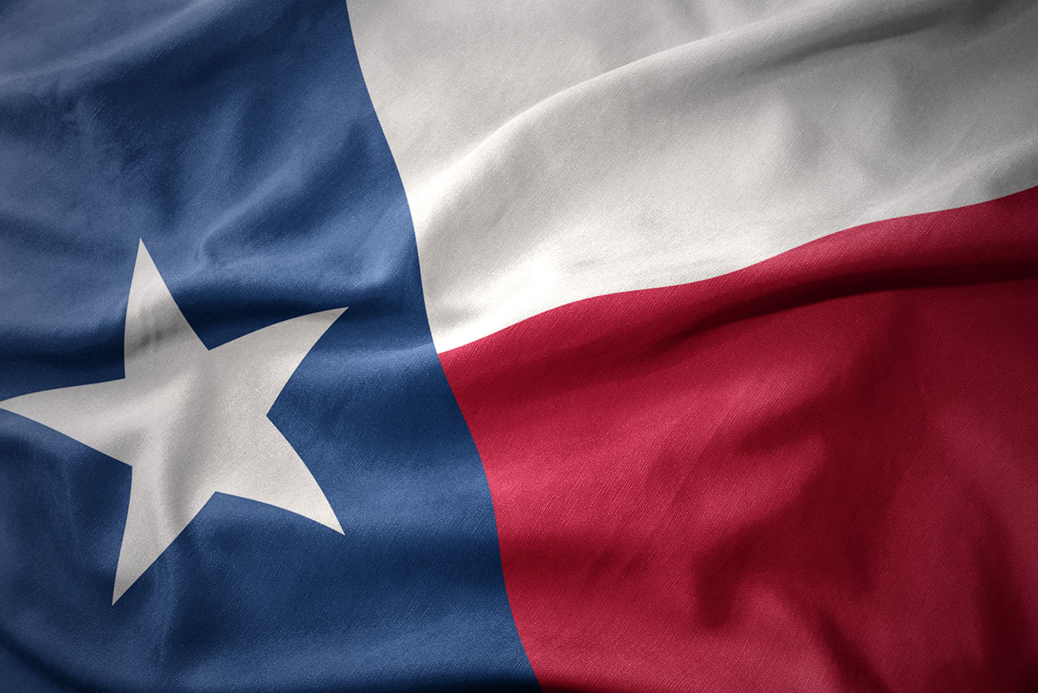 Close up of Texas state flag with a white star on a blue field next to wide white and red stripes