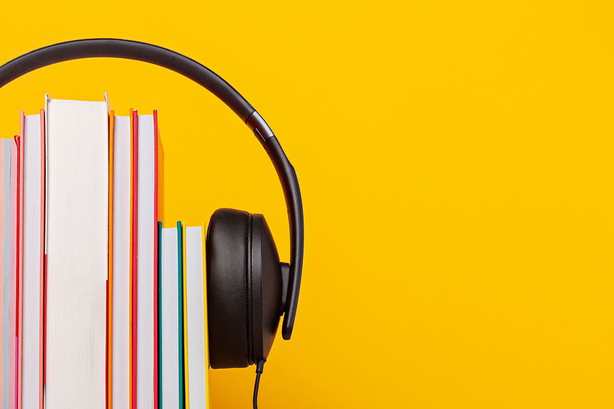 Over the ear headphones placed over a stack of hardcover books on a bright yellow background