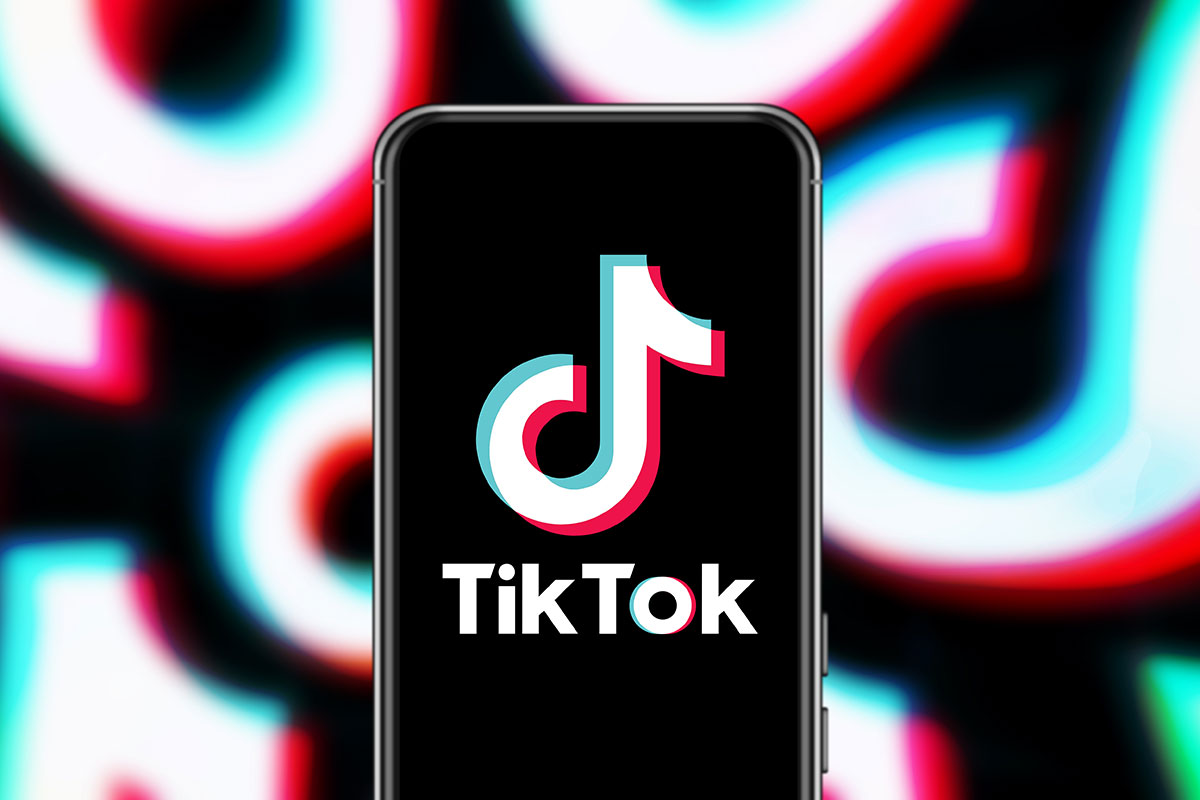 Black phone with TikTok logo in front of background featuring repeating TikTok logos