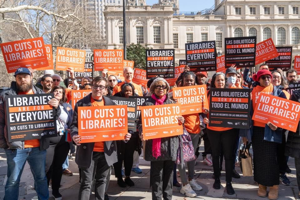 Crowd of people outside the New York Public Library holding signs reading Libraries are for Everyone and No Cuts to Libraries