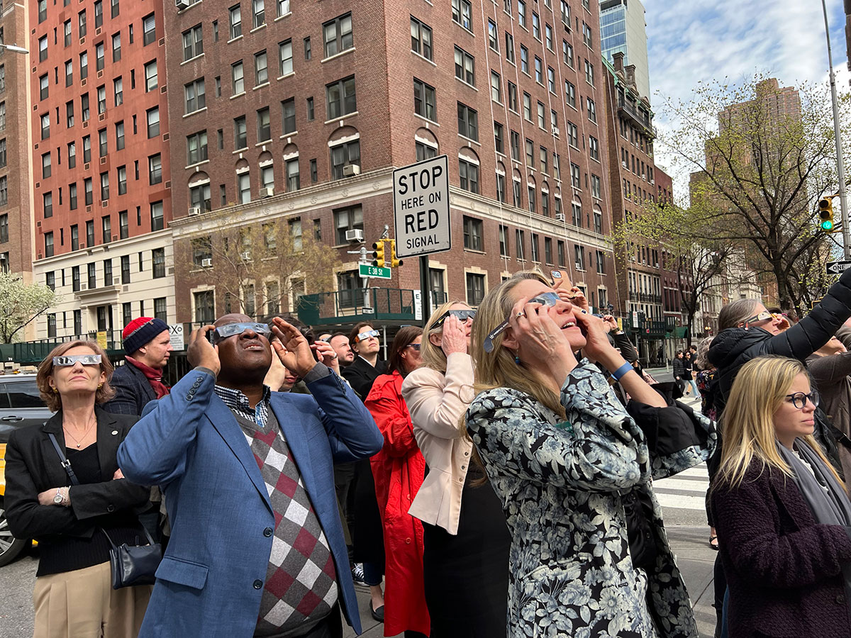 IAF attendees gather in the center island on Park Avenue and hold eclipse glasses up to their eyes