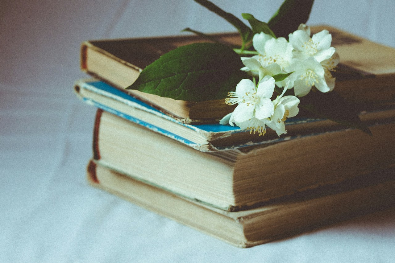 A stack of four books with flowers on top on a white tablecloth.