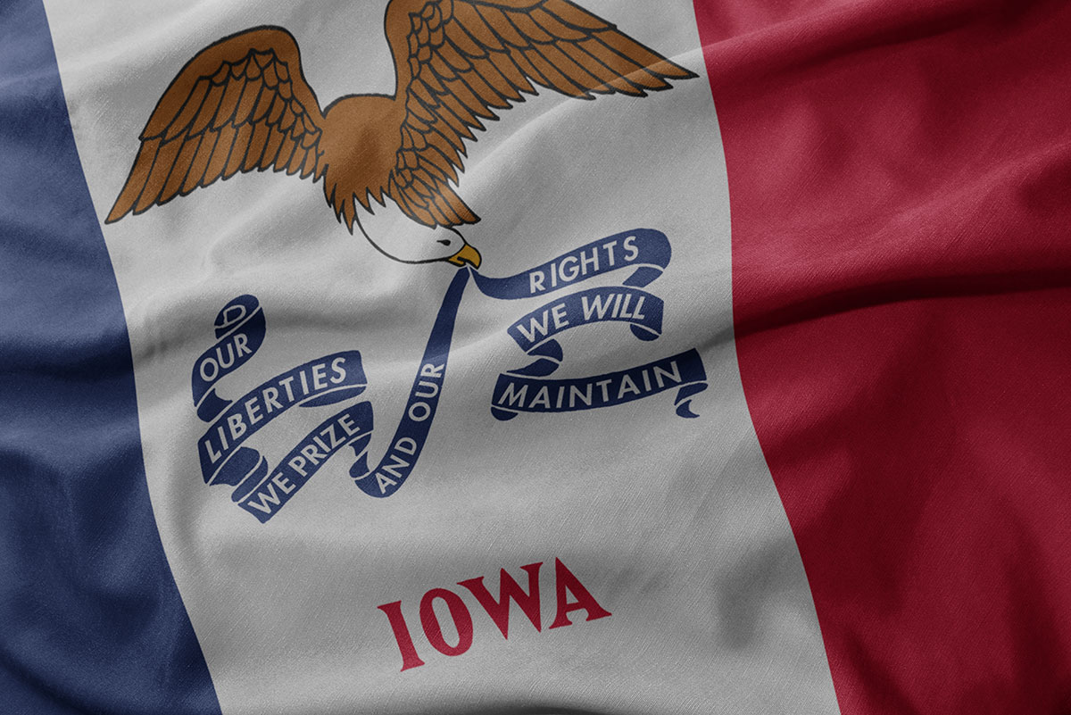 Close up of Iowa state flag: Blue, white, and red fields featuring the name Iowa and a bald eagle holding banner reading Our Liberties We Prize and Our Rights We Will Maintain