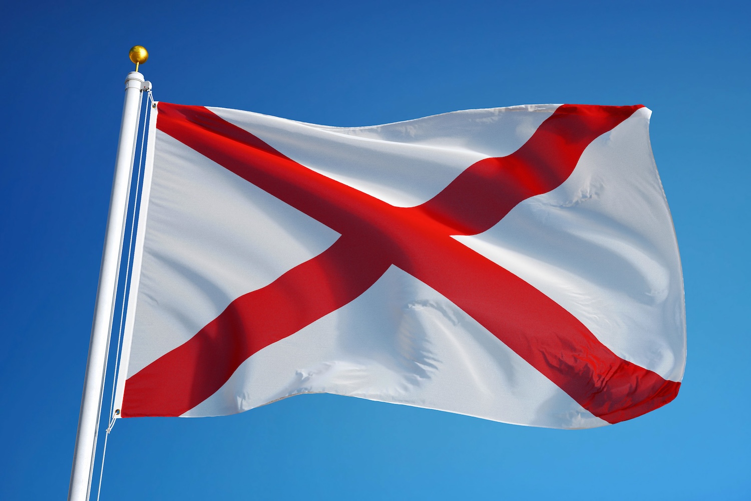 Alabama state flag featuring a red X on a white field, shown against a bright blue sky