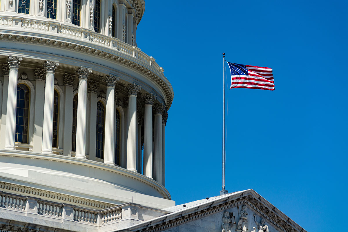 Closeup of the U.S. Capitol dome in Washington, D.C., with a U.S. flag flying in the foreground, by day